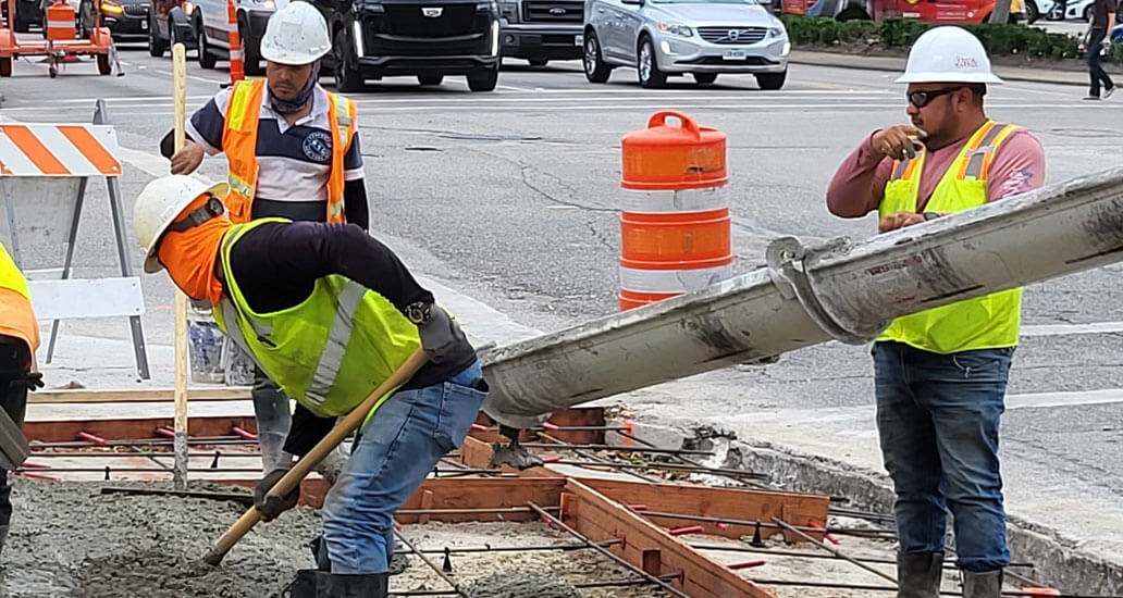 Construction workers filling area with concrete as mixing truck pours.
